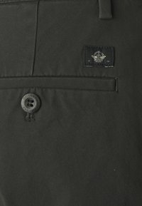 Czarne chinosy o gładkiej fakturze, z zapięciem na guzik oraz metką z logo na tylnej kieszeni.