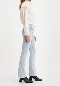 Světlé modré rozšířené džíny s vysokým pasem, se klasickým designem pěti kapes a mírně vybledlým vzhledem. V kombinaci s bílou košilí na knoflíky.