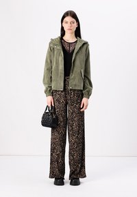 Grønn kordfløyelsjakke med hette, svart blondetopp, leopardprint vide bukser, svart håndveske, og kraftige svarte sko.