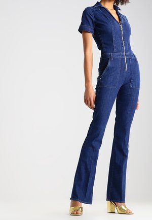 Donkerblauwe spijkeroverall met ritssluiting, korte mouwen en uitlopende pijpen; voorzien van voorzakken en een aangesloten silhouet.