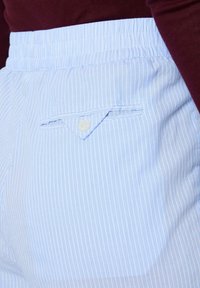 Šviesiai mėlynos dryžuotos šortai su elastinga juosmens juosta. Šone kišenė su smailiu atvartėliu ir sagos užsegimu. Lygios medvilnės tekstūra.