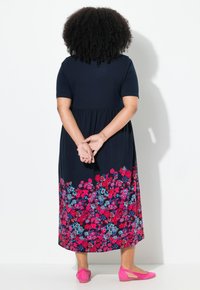 Marineblaues Kleid mit kurzen Ärmeln, elastischem Bund und Blumenmuster in Rosa und Blau am Saum. Kombiniert mit rosa Ballerinas.