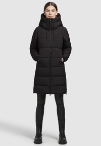 Abrigo largo negro de plumas con cierre de cremallera, cuello alto y capucha con cordón ajustable. Presenta un diseño acolchado y cremalleras laterales.