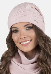 Gorro de punto rosa con líneas texturizadas y adornos similares a perlas. Acompañado por una bufanda rosa, que presenta una textura suave y lisa.