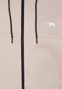 Felpa beige con zip nera e coulisse, caratterizzata da una finitura testurizzata e da una piccola etichetta logo sul lato sinistro superiore.