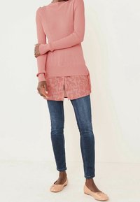 Roze geribbelde trui over een roze gebloemde blouse, gecombineerd met donkere blauwe skinny jeans en lichtroze ballet flats.
