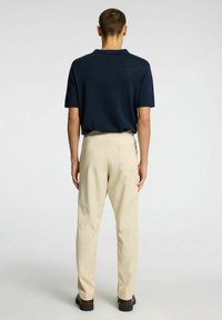 Marinblå kortärmad pikétröja i kombination med ljusbeiga byxor. Byxorna har en bakficka och elastisk midja, vilket ger en avslappnad passform.