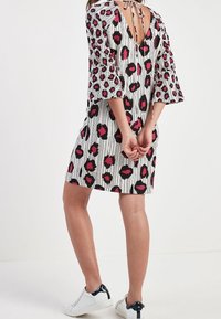 Robe à manches courtes blanche avec des rayures verticales noires et un motif de lèvres roses, dotée d'un dos en V et d'un lien ajustable. Associée à des baskets blanches.