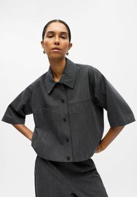 Graues kurzärmliges Button-Down-Hemd mit Kragen, ausgestattet mit einem strukturierten Stoff und zwei Fronttaschen. Schlanker Schnitt mit verkürztem Design.