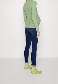 Grön veckad långärmad topp som är kombinerad med mörkblå skinny jeans och limegröna ankelstövlar, med en tajt siluett och vertikal textur.