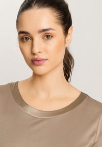 Top beige con una tela suave y ligera, con un cuello en un tono beige más oscuro y acabados satinados. El diseño incluye un cuello redondo.
