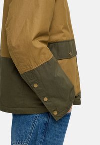 Kurtka w blokach kolorystycznych z brązową górną częścią, ciemnozieloną dolną częścią, zatrzaskami oraz teksturowanym wykończeniem materiału.