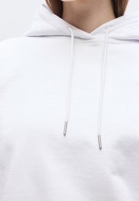 Gros plan d'une personne portant un sweat à capuche blanc avec des cordons blancs pendant à l'avant.