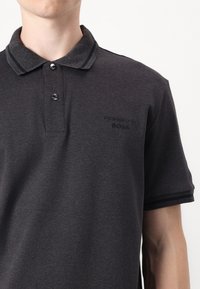 Mørkegrå polo t-skjorte laget av myk stoff, med en ribbet krage med kontraststriper, to knapper og brodert logo på brystet.