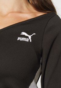 Top lungo a maniche nere a coste con design off-shoulder, logo Puma ricamato bianco e pannelli laterali bianchi a contrasto.