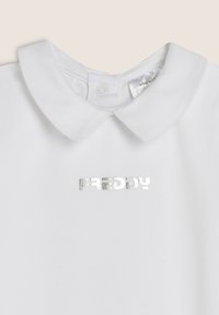 Polo bianca con colletto classico, caratterizzata dal logo "FREDDY" in argento. Realizzata in tessuto morbido, con chiusura a scatto sul colletto.