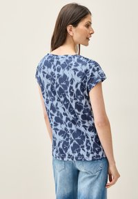 Camiseta de manga corta, teñida en azul marino y azul claro, con un corte relajado y detalles de hombros fruncidos, hecha de una tela suave y ligera.