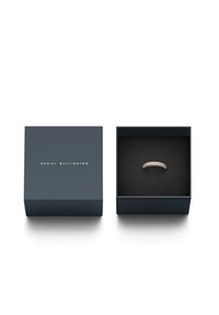 Temno modra škatla z zlatim napisom "DANIEL WELLINGTON"; vsebuje srebrn prstan s ukrivljenim dizajnom in številnimi majhnimi vgrajenimi dragulji.