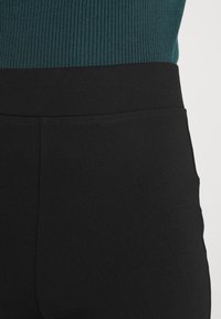 Leggings pretos de cintura alta feitos de um tecido elástico, com uma textura suave e um design justo. Sem hardware visível ou padrões.