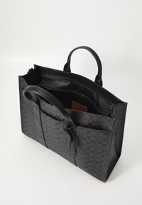 Black leather tote bag with a textured fabric exterior, dual handles, zippered interior, and external pockets for added organization.