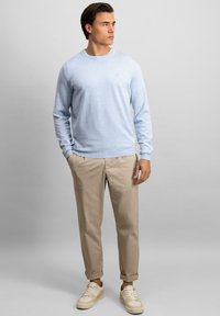 Lyseblå genser med rund hals, kombinert med beige tapered bukser og kremfargede sneakers. Stoffet er mykt og gir en avslappet passform.