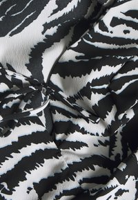 Svart och vit tyg med ett djärvt djurmönster och blå accentfärger. Slät textur med samlad detaljer, vilket skapar mjuka draperingar.