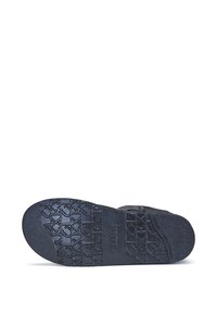 Černé sandály s texturovanou gumovou podrážkou s geometrickými vzory. Nastavitelný pásek dokresluje minimalistický design.