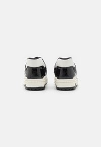 Sneakers bianco e nero con finitura in pelle verniciata lucida, il design presenta un colletto alla caviglia imbottito e una suola in gomma testurizzata.