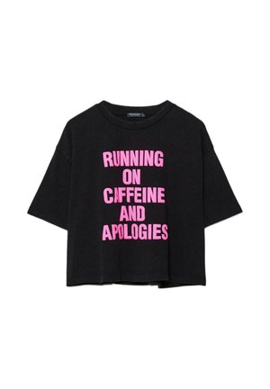 T-shirt noir surdimensionné avec un texte rose vif "RUNNING ON CAFFEINE AND APOLOGIES" centré sur le devant.