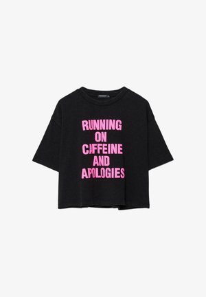 T-shirt noir surdimensionné avec un texte rose vif "RUNNING ON CAFFEINE AND APOLOGIES" centré sur le devant.