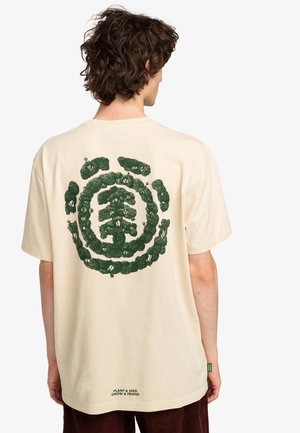 T-shirt in cotone color crema con una grande grafica circolare verde sul retro, con il testo "PIANTA UN SEME, CRESCI UN AMICO" all'orlo.