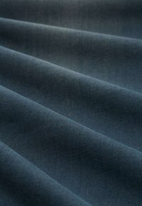 Dunkelblauer Stoff mit glatter Textur, der mehrere gefaltete Lagen aufweist. Die Webart ist dicht, was die Haltbarkeit und Stärke des Materials erhöht.