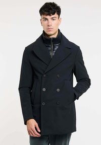 Donkerblauwe peacoat met een dubbelzijdig ontwerp, grote kleppen, twee voork genaaide zakken en een hoge kraag over een gewatteerde binnenlaag.