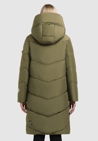 Abrigo de plumas color verde aceituna con una gran capucha, costuras en forma de chevrón y mangas largas. Presenta una etiqueta de logo cerca del dobladillo. Textura suave.