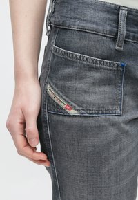 Γκρι τζιν παντελόνι με πίσω τσέπη που φέρει ορατή ετικέτα. Οι ραφές είναι μπλε. Το ύφασμα φαίνεται μαλακό με ελαφρώς ξεθωριασμένη υφή.