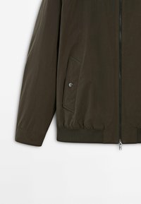 Olijfgroene, lichtgewicht bomberjack met ritssluiting, elastische manchetten en een zijzak met drukknoopdetail. Soepele textuur.