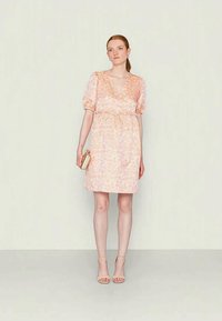 Vestido floral rosa com mangas curtas bufantes, decote em V, cintura ajustada e saia ligeiramente evasé. Usado com sandálias de salto bege.