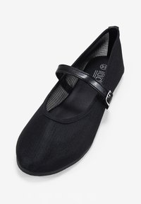 Zapato plano de tela negra con punta redondeada, una delgada correa negra en el empeine y un interior texturizado. Diseño ligero.