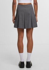 Harmaa laskostettu hame, jossa on levenevä muotoilu, mukautuva vyötärö ja sileä pinta. Yhdistetty valkoisiin sukkiin ja muhkeisiin mustiin kenkiin.