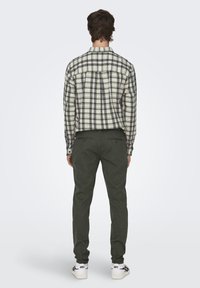 Geruite flanellen shirt in roomkleur en marineblauw, gecombineerd met smal gesneden donkergroene broek. Katoenen stof met een gladde textuur en knoopdetails.