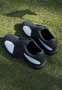 Black and white sports shoes with laces placed on green grass surface, viewed from above.