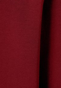 Nahaufnahme eines burgunderfarbenen Stoffes mit feiner Stricktextur und einem sanften Faltenwurf, der eine schattierte vertikale Linie erzeugt.