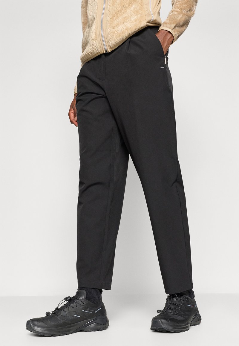 Czarne, zwężające się spodnie o gładkiej fakturze, z kieszeniami bocznymi i minimalnymi detalami, w zestawieniu z czarnymi butami turystycznymi.