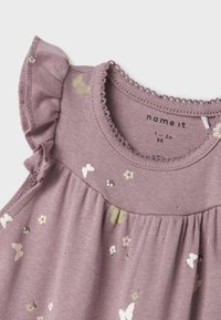 Top de algodón morado con detalle de hombros con volantes, que presenta un estampado de flores y mariposas en blanco roto y verde claro, diseño fruncido en la cintura.