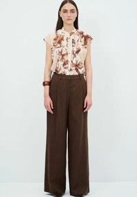 Lichtblouse met bloemenprint in bruintinten, met een ruchesnek en korte mouwen, gecombineerd met hoge taille, brede bruine broeken.
