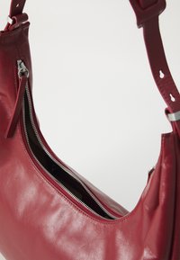 Red leather shoulder bag with silver zipper partially open and adjustable strap with holes and buckle.