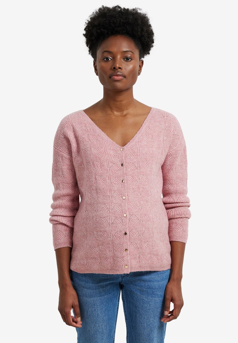 Helles rosa gestricktes Cardigan mit V-Ausschnitt, strukturiertem Muster und goldenen Knöpfen. Lange Ärmel und taillierte Passform, kombiniert mit lässigen Jeans.