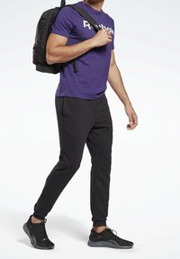 Purple short-sleeve Reebok t-shirt, black tapered sweatpants, and black athletic shoes. The individual is carrying a black backpack.