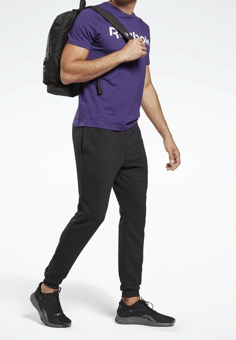Purple short-sleeve Reebok t-shirt, black tapered sweatpants, and black athletic shoes. The individual is carrying a black backpack.
