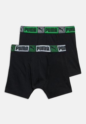 Dva páry černých boxerů Puma s elastickými pasy, jeden pás zeleno-černý, druhý bílý se zeleným, oba s logem Puma.